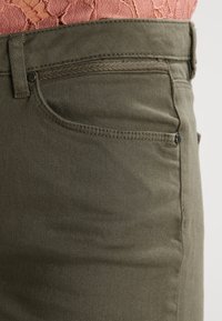 Pantalones verde oliva con una suave mezcla de algodón, un bolsillo frontal con un botón de metal y detalles trenzados a lo largo de la cintura.
