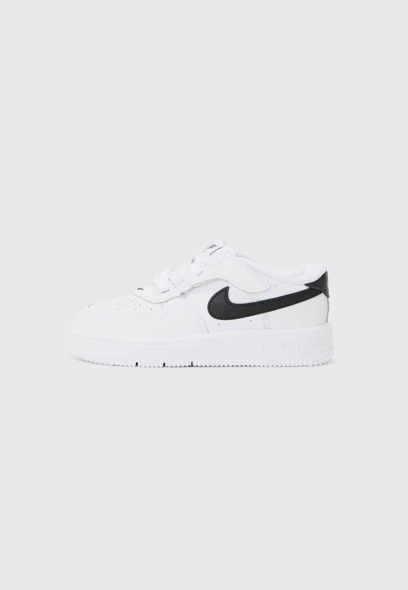 Ténis Nike brancos com um swoosh preto, apresentando um cabedal em couro liso, fecho com atacadores, biqueira perfurada e sola grossa em borracha.