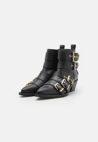 Botines de cuero negro con punta afilada, múltiples correas horizontales, hebillas doradas y plateadas, y un tacón bajo y apilado.