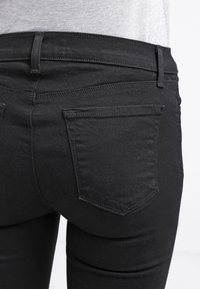 Black denim jeans with a fitted design, featuring standard back pockets and subtle stitching details. Smooth texture with a slight sheen.
