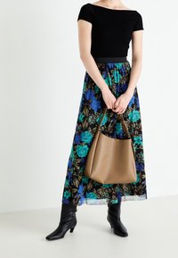 Svart ribbad topp, blommig maxikjol med blå och gröna blommor, brun handväska och knähöga svarta stövlar. Enkelt design och mjuk textur.