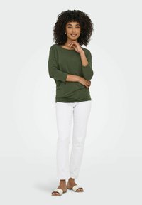 Maglione verde oliva a maniche lunghe con vestibilità comoda, abbinato a pantaloni bianchi e sandali chiari. Design semplice e casual, senza fantasie.