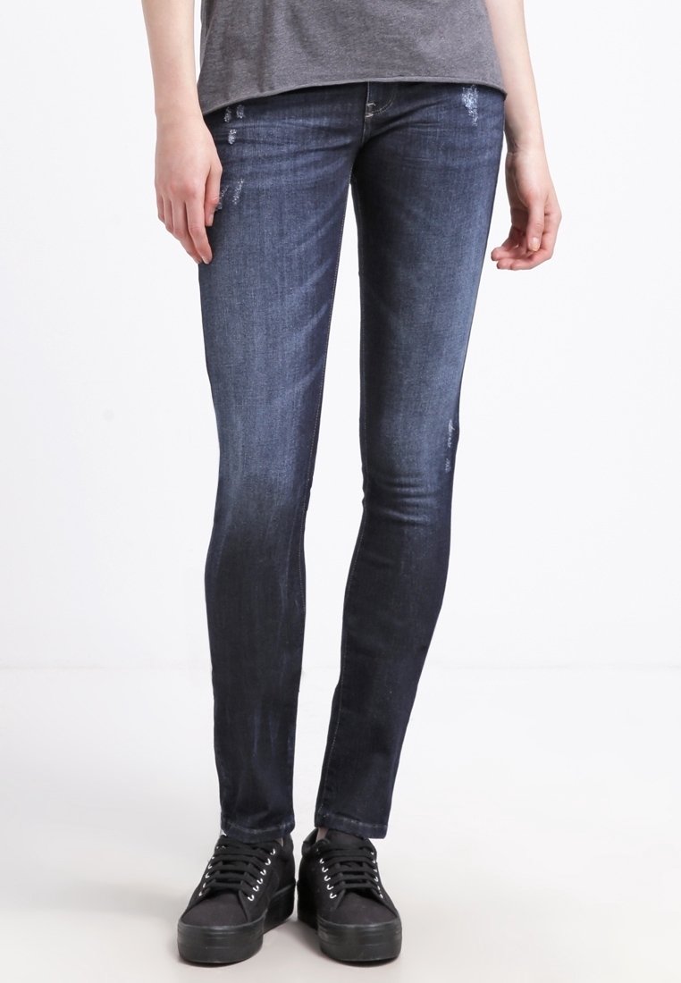Jeans skinny blu scuro con una texture sbiadita e un leggero effetto usurato, abbinati a sneakers nere con lacci piatti e suole rialzate.