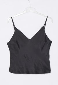 Caraco en satin noir sans manches avec fines bretelles suspendu à un cintre en plastique transparent sur fond blanc.
