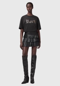 Mustan puuvillat-paidan, jossa on graafinen printti, on yhdistetty mustaan, poimutettuun aitoon nahkaan valmistettuun mini-hameeseen ja polven ylle ulottuviin mustiin nahkasaappaisiin.