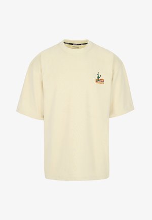 Cremefarbenes T-Shirt mit kurzen Ärmeln, kleinem Kaktus-Print und wellenförmigen Streifen auf der oberen linken Brust.