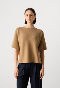 Top scurt maro cu mânecă, cu un finisaj texturat și un decolteu rotund, asortat cu pantaloni bleumarin cu dungi verticale. Design simplu, modern.