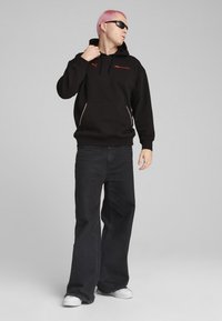 Haut à capuche noir avec des accents rouges, doté d'une poche avant et d'une capuche avec cordon. Associé à un jean noir ample et des baskets blanches.