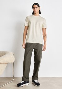 T-shirt en coton beige à manches courtes, associé à un pantalon cargo vert olive et des baskets noires. Texture lisse avec un design ajusté.