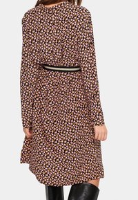 Vestito nero con maniche lunghe, caratterizzato da un piccolo motivo floreale nei toni del rosa e dell'arancio, messo in risalto da una cintura nera in vita.