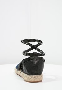 Musta espadrille-sandaalit, joissa on kudottu juuttipohja, ristiin menevä hihnadesign neliön muotoisilla niiteillä ja teksturoitu nahkapinta.