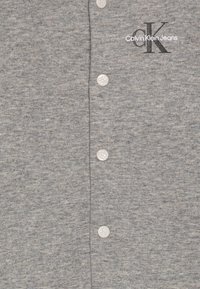 Cardigan din bumbac gri, cu închidere cu butoane de culoare gri deschis. Logo-ul brodat "Calvin Klein Jeans" și emblema "CK" sunt ilustrate.