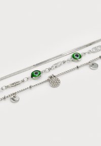 Conjunto de joyería de plata que incluye tres cadenas. Una tiene acentos de ojos verdes, otra tiene un charm redondo con piedras de imitación, y la tercera es una cadena serpiente lisa.
