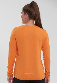 Langärmliges Sportoberteil in leuchtendem Orange, aus strukturiertem Stoff mit rundem Halsausschnitt, seitlichen Schlitzen und reflektierenden Details am hinteren Saum.