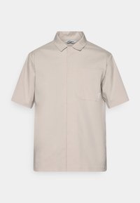 Short-sleeve collared shirt in light beige cotton, features a single chest pocket, clean lines, and subtle stitching details.