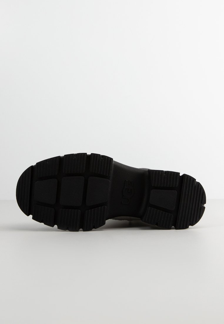 Schwarze Gummisohle mit strukturiertem Grip-Muster. Verfügt über eine abgerundete Zehenpartie, tiefe Eindellungen und ein geprägtes Logo. Glatte Oberfläche mit robuster Bauweise.