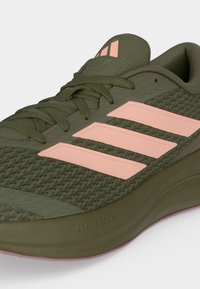 Αθλητικό παπούτσι ελιάς με ροζ ρίγες Adidas, κορδόνια, μαλακή σόλα με την ένδειξη "Cloudfoam" και επάνω μέρος από αεριζόμενο πλέγμα.