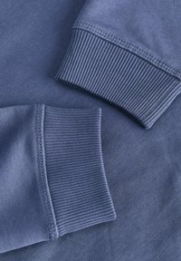 Gros plan de deux manches de sweat-shirt bleues avec des poignets côtelés et des coutures visibles sur un tissu doux.