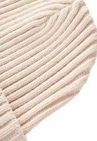 Helle beige Strickmütze mit gerippter Textur und umgeschlagenem Saum. Das Material ist weich, mit ausgeprägten horizontalen Linien, die Tiefe verleihen.