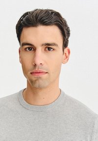 Szary sweter z okrągłym dekoltem, miękka faktura, dopasowany krój. Jasne tło, skoncentrowany obiekt z krótkimi ciemnymi włosami i neutralnym wyrazem twarzy.