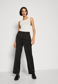 Black wide-leg trousers and a light knit sleeveless top. The outfit features clean lines and a modern fit, complemented by sleek black loafers.