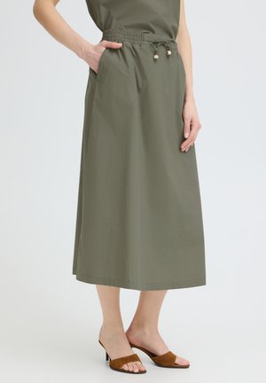 Oliwkowa spódnica midi z elastycznym pasem i sznurkiem, kieszenie po bokach, noszona z brązowymi sandałami na obcasie z odkrytymi palcami.