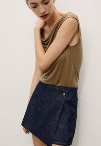 Olive draped top with short sleeves paired with a dark denim A-line mini skirt featuring a snap closure and a side wrap design.