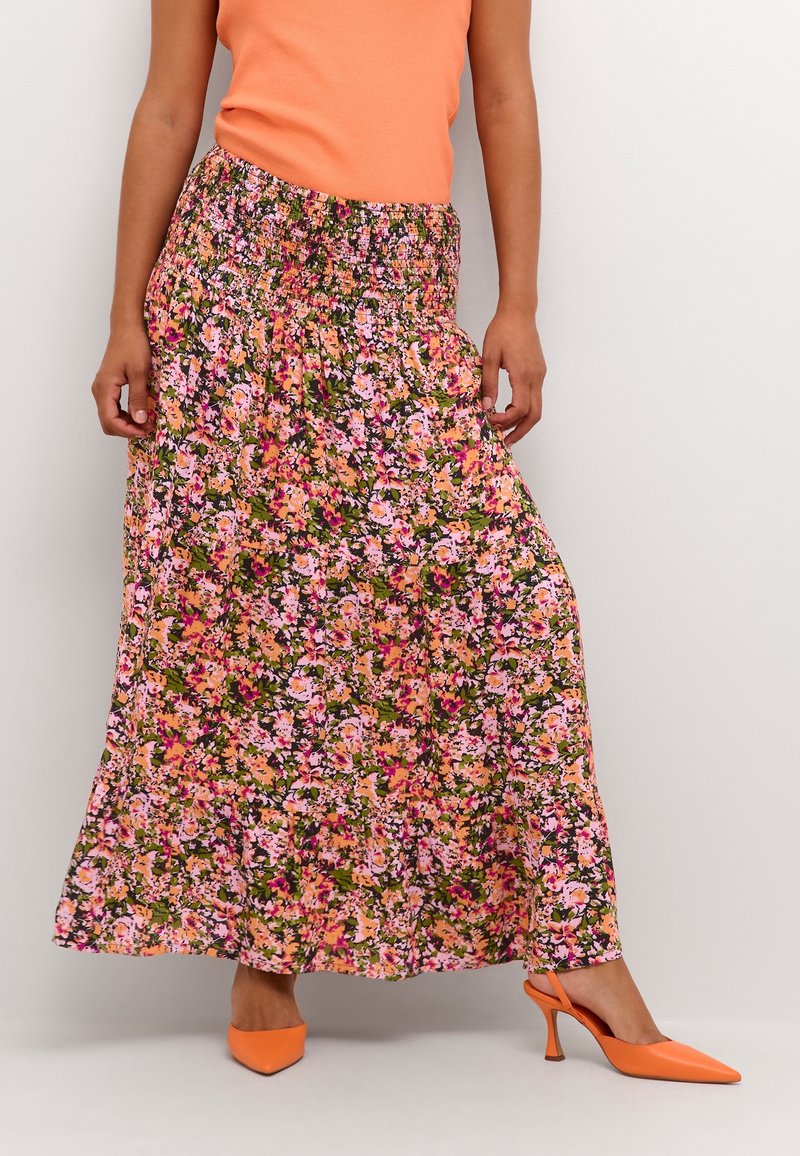 Jupe longue fleurie avec une taille smockée, ornée de fleurs roses et orange sur un fond vert. Associée à des escarpins à bride arrière orange.