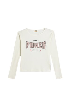 Chemise blanche à manches longues avec une texture côtelée, ornée d'un texte noir et rouge audacieux "LA MUSIQUE EST UN POUVOIR" et des accents d'éclairs.