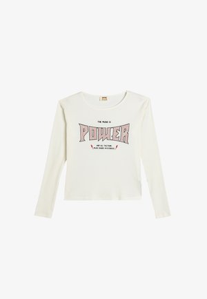 Witte langemouwen shirt met ribbelstructuur, voorzien van gedurfde zwarte en rode tekst "DE MUZIEK IS KRACHT" en bliksemschichtaccenten.