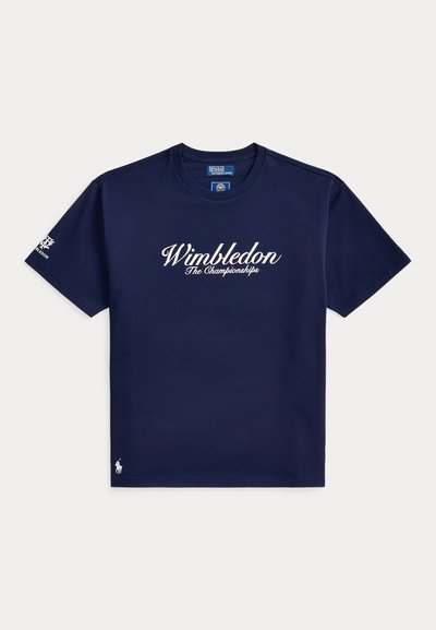 Μπλε σκούρο κοντομάνικο T-shirt με το κείμενο "Wimbledon The Championships" στο μπροστινό μέρος, λογότυπο κάτω αριστερά και έμβλημα του Wimbledon στο αριστερό μανίκι.