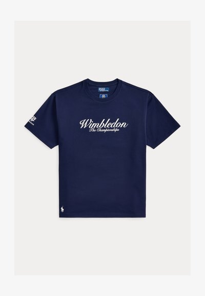Μπλε σκούρο κοντομάνικο T-shirt με το κείμενο "Wimbledon The Championships" στο μπροστινό μέρος, λογότυπο κάτω αριστερά και έμβλημα του Wimbledon στο αριστερό μανίκι.