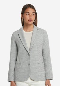 Grå texturerad kavaj med slag, två framfickor och två knappar. Slim fit-design, visad på en modell som bär en ljus topp.