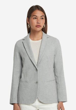 Grijze textuur blazer met poilapjes, twee voorkruiden en twee knopen. Slanke pasvorm, getoond op een model met een lichte top.