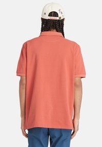 Korallfärgad kortärmad polo med lös passform, i bomull och med platt krage. Baksidan har en rak fåll och minimal detaljering.