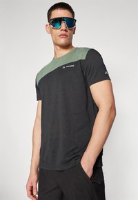 T-shirt sportivo nero con una sezione superiore verde. Realizzato in tessuto leggero, presenta un logo sul petto e maniche corte.
