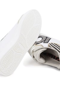 Zapatillas blancas con una suela texturizada, que presentan un upper de patrón en blanco y negro, acentos dorados y un forro interior suave.