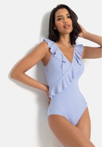 Maillot de bain une pièce rayé bleu et blanc avec des accents en volants le long de l'encolure et des épaules, présentant un décolleté en V et une texture lisse.