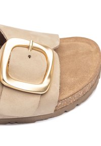 Sandale en suède beige avec une large sangle, dotée d'une grande boucle carrée en or. La semelle intérieure est rembourrée avec une semelle en liège texturée.