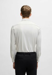 Lange mouw shirt in licht crème met een subtiele textuur, voorzien van een klassieke kraag en knoopmanchetten, gecombineerd met zwarte broek.