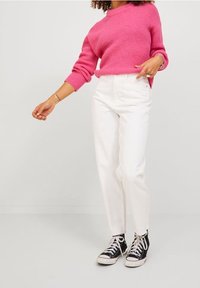 Maglione rosa lavorato a maglia con maniche lunghe, abbinato a jeans bianchi a gamba dritta e sneakers nere alte. Outfit semplice e informale.