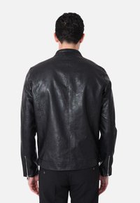 Giacca di pelle nera con una texture liscia, polsini con zip e un design aderente. Dettagli di cucitura visibili e colletto classico.