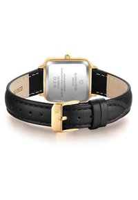 Montre avec bracelet en cuir noir et un boîtier rectangulaire en métal doré. Présente un fond en acier inoxydable argenté poli avec des gravures. Fermeture à boucle.
