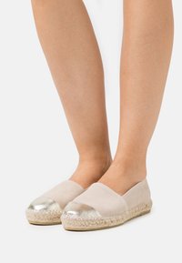 Beige Wildleder-Espadrilles mit einer metallic-silbernen Zehenkappe, Jutesohle und minimalistischem Design. Flacher und atmungsaktiver Stil für die Freizeit.