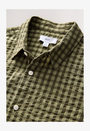 Vihreä ruudullinen lyhythihainen paita, jossa on teksturoidusta kankaasta tehty materiaali, napillinen edusta ja valkoinen merkintä, jossa on tuotemerkin nimi "NEXT".