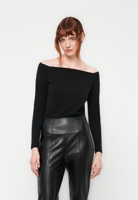 Top nero off-shoulder a maniche lunghe realizzato in tessuto morbido, abbinato a pantaloni neri in ecopelle a vita alta con dettagli delle cuciture.