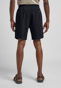 Shorts neri con una cintura elastica, tasche laterali e posteriori, realizzati in tessuto leggero. Indossati con sandali marroni, che mostrano le gambe da dietro.