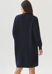 Robe pull surdimensionnée bleu marine avec des manches longues, un col rond et une texture douce, tombant à mi-thigh.