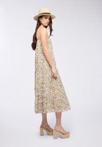 Maxi dress beige a fantasia con spalline sottili, tessuto biologico e design a strati. Abbinato a sandali con tacco spesso color sabbia e un cappello di paglia.