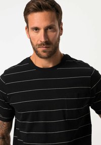 Camiseta de manga corta a rayas negras hecha de algodón. Presenta rayas horizontales blancas y un bolsillo en el lado izquierdo del pecho. Textura suave.